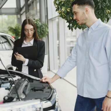 Man and woman examining car engine in dealership service area, focused on vehicle maintenance and functionality.
