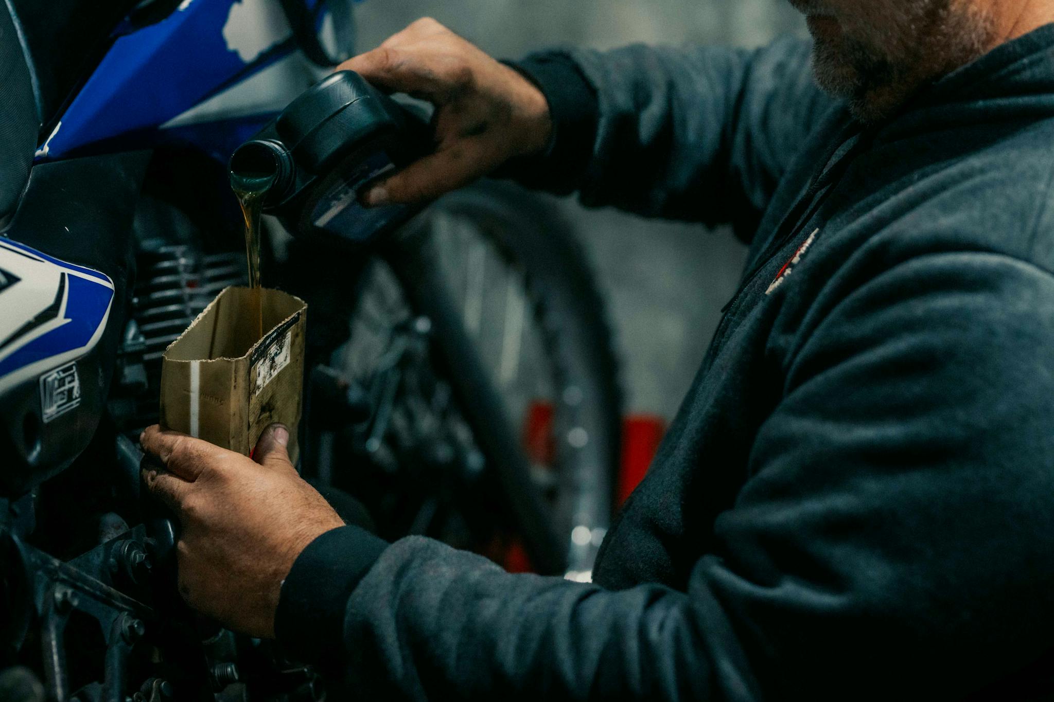 Mechanic pouring oil in a motorcycle in a dimly lit garage, emphasizing maintenance.