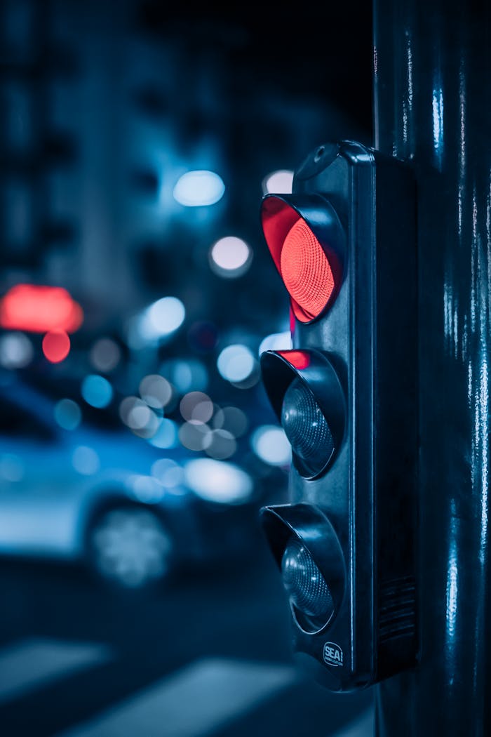A traffic light glows red on a bustling Rabat street at night with blurred city lights.